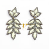 A pair of silver and white leaf-shaped earrings with a gold-colored inscription.