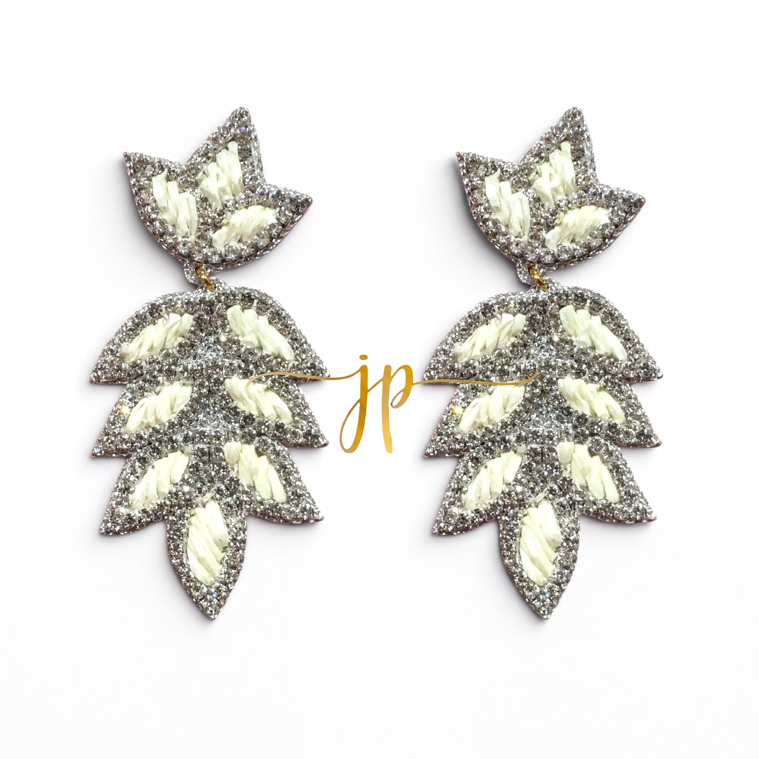 A pair of silver and white leaf-shaped earrings with a gold-colored inscription.