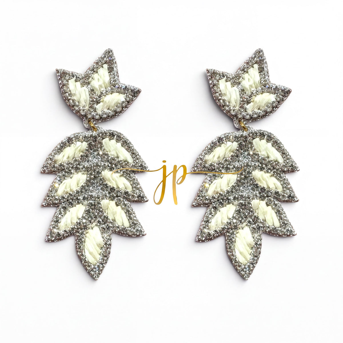 A pair of silver and white leaf-shaped earrings with a gold-colored inscription.