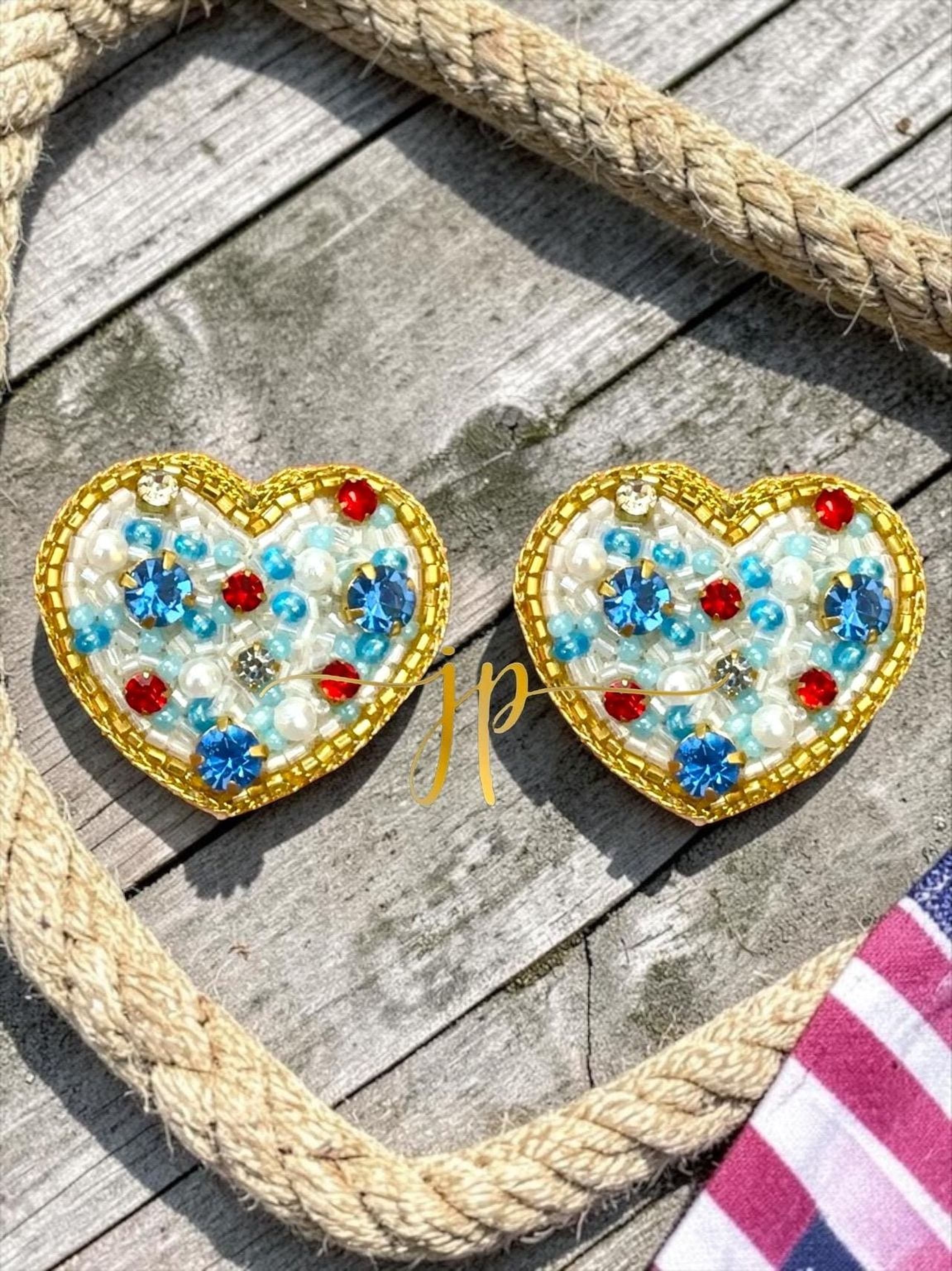 two heart-shaped earrings with gold and blue beads, placed on a wooden surface.